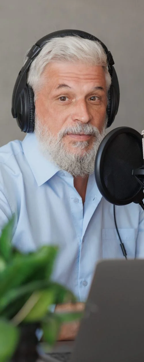 older man with gray hair irecording podcast in recording studio with microphone and headphones. senior radio presenter or interviewer. recording audio content for social media online